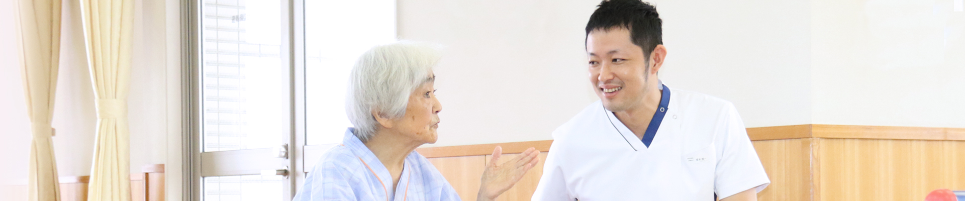 介護職員と入居者が会話する様子。明るい共用スペースでの交流風景。